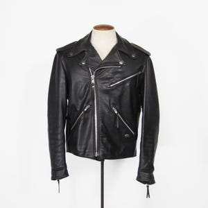 May include: Black leather jacket with a classic motorcycle style. Features a notched collar, asymmetrical zipper closure, and multiple zippered pockets. The jacket is displayed on a mannequin against a white background.