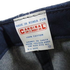 Puede incluir: Una etiqueta blanca con texto azul que dice "MADE IN KOREA FOR: CARDINAL CAP & JACKET CO. 100% COTTON GRUNDY, VA 24614 PHONE: 703/935-4545 ONE SIZE FITS ALL S/#: 527F" con un c&iacute;rculo azul que contiene el n&uacute;mero 12.