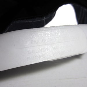Puede incluir: Primer plano de una etiqueta blanca con el texto "ARDINA CAP & JACKET" y "GRUNDY, VA PHONE 703/937-****".