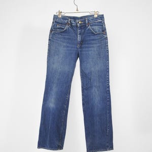 Op de afbeelding: Een paar blauwe denim jeans hangend aan een kledinghanger. De jeans heeft een klassieke rechte pijp en een lichte wassing.