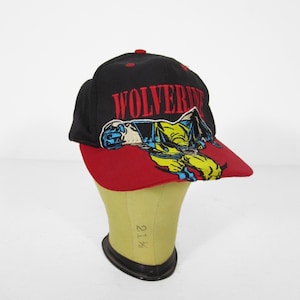 May include: Black baseball cap with a red brim featuring the word "WOLVERINE" in red block letters. The cap has a graphic of the Wolverine character in yellow and blue.