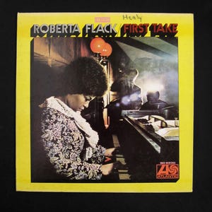 May include: Album cover for Roberta Flack's "First Take" on a yellow background. The album art features a photo of Roberta Flack playing a piano. The album cover has the Atlantic Records logo and the text "Roberta Flack First Take".