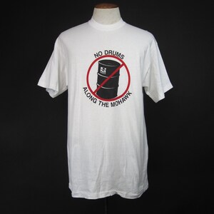 May include: White t-shirt with a black and red graphic of a barrel with a red slash through it. The text "NO DRUMS ALONG THE MOHAWK" is printed around the graphic.