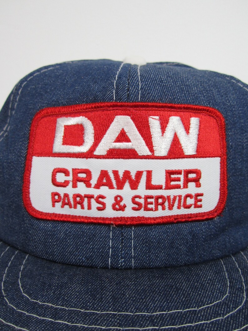 Puede incluir: Un gorro de camionero de mezclilla azul con un parche rojo y blanco que dice "DAW CRAWLER PARTS & SERVICE".