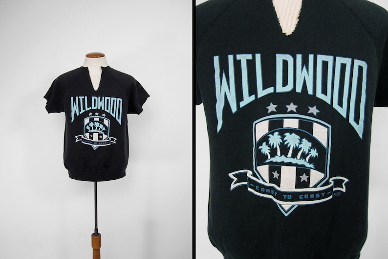 May include: Black short-sleeved sweatshirt with a blue and white graphic of a shield with palm trees and the text "WILDWOOD - COAST TO COAST -"