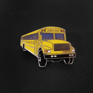 Puede incluir: Un pin de autobús escolar amarillo con neumáticos negros y ribete plateado. El pin tiene las palabras "SCHOOL BUS" encima del parabrisas. El autobús tiene un diseño detallado con ventanas y faros.