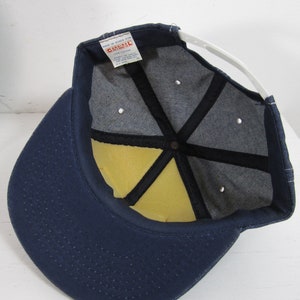 Puede incluir: Una gorra de b&eacute;isbol de mezclilla azul con una correa ajustable blanca y un interior de espuma amarilla. La gorra tiene una etiqueta que dice "Cardinal" y "Made in Korea for Cardinal Sportswear Co."