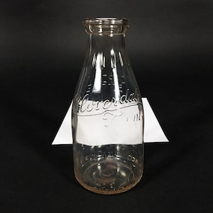 Puede incluir: Una botella de leche de vidrio transparente con un tinte rosado y las palabras "Cloverdale Farm" grabadas en el lateral.