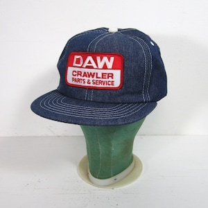 May include: A blue denim baseball cap with a red and white patch that reads "DAW CRAWLER PARTS & SERVICE".