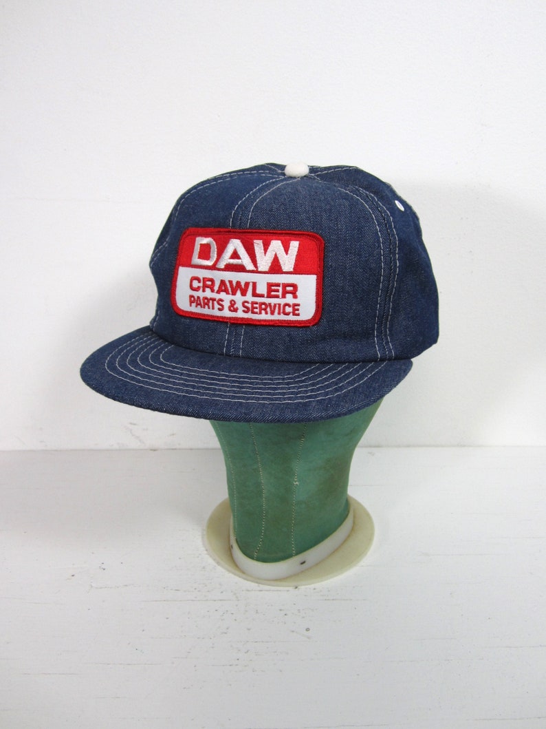 Puede incluir: Una gorra de b&eacute;isbol de mezclilla azul con un parche rojo y blanco que dice "DAW CRAWLER PARTS & SERVICE".