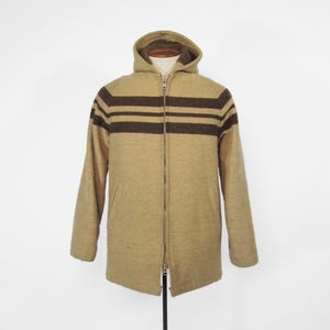 Könnte beinhalten: Beige Kapuzenjacke mit durchgehendem Reißverschluss und zwei dunkelbraunen horizontalen Streifen auf Brust und Oberarmen. Die Jacke wird auf einer Schaufensterpuppe vor weißem Hintergrund präsentiert. Die Jacke hat lange Ärmel und eine Kapuze.