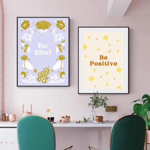 May include: Two framed art prints with inspirational messages. The left print has a lavender background with the words "Be Kind" and floral illustrations. The right print has a cream background with the words "Be Positive" and yellow flower illustrations.