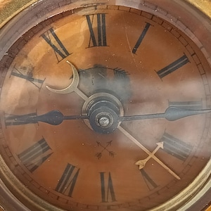 May include: Close-up of a vintage brass clock with a circular face. The clock features Roman numerals and ornate hands. The face has a warm, aged tone, and the clock is encased in a gold-colored frame. The hands point to approximately 10:10.