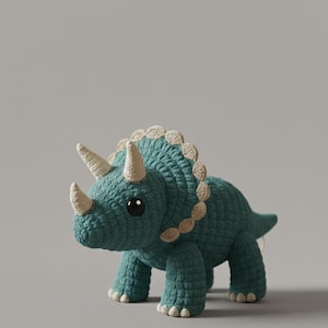 May include: A teal crochet triceratops dinosaur with three cream-colored horns and a frill. The handmade stuffed animal has large black eyes and is standing on four legs. The dinosaur is a soft toy.