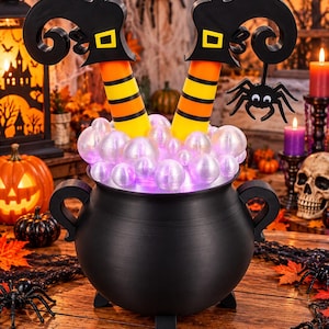 May include: A black cauldron decoration featuring two legs wearing orange and yellow striped socks and black pointed boots sticking out of the top. The cauldron is filled with glowing, iridescent white bubbles and includes a black spider hanging from one boot.