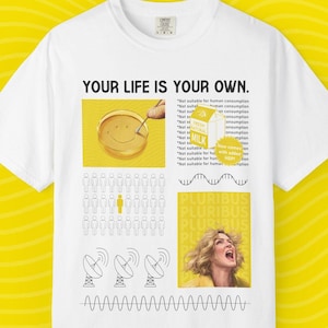 May include: White t-shirt with a graphic design featuring the text "YOUR LIFE IS YOUR OWN." The design includes a smiling face, a milk carton, a crowd of people, and a woman yelling. The shirt has a crew neck.