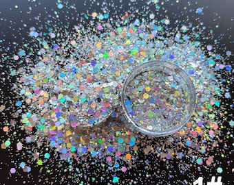 May include: A clear plastic jar filled with holographic silver glitter in various hexagonal and circular sizes, with additional loose glitter scattered around the base. The text 1# is printed in white in the bottom right corner of the image.