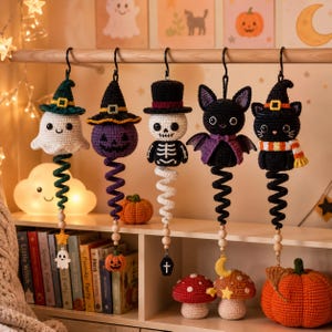 May include: Five hanging crochet ornaments featuring a ghost with a green hat, a purple pumpkin with a black hat, a skeleton with a top hat, a black bat with purple wings, and a black cat with a witch hat, each with a spiral tail and wooden beads.