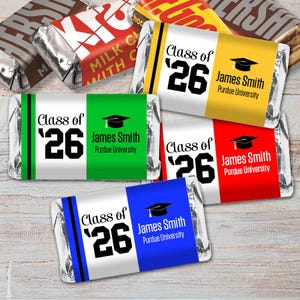 May include: Assorted candy bars with personalized wrappers. Each wrapper features the text "Class of '26", a graduation cap graphic, and the name "James Smith" with "Purdue University". The wrappers are in various colors.