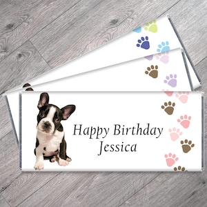 May include: Three white chocolate bar wrappers with a brown and white French bulldog puppy image on the front. The wrapper has the text "Happy Birthday Jessica" and a border of brown and pink paw prints.