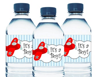 May include: Three clear plastic water bottles with blue and white striped labels. The labels feature a red airplane with a white star and the text "It's a Boy!"