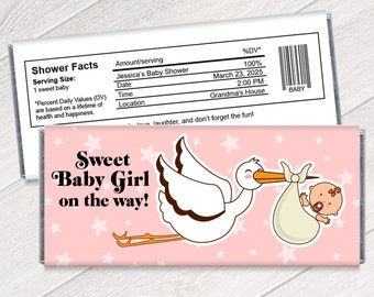 May include: Pink and white chocolate bar wrapper with a stork carrying a baby girl. The wrapper has the text "Sweet Baby Girl on the way!" and stars. The back of the wrapper has a nutrition facts label with the text "Jessica's Baby Shower" and "Grandma's House".