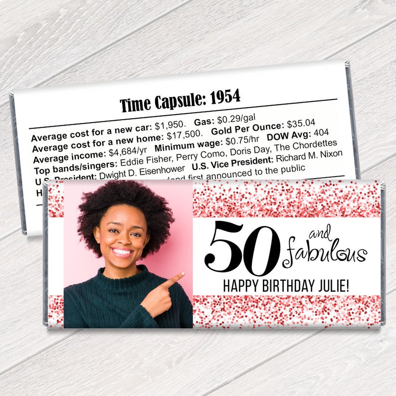 K&ouml;nnte beinhalten: Personalisierte Schokoriegelverpackung mit einem Foto einer Frau, dem Text "50 and fabulous" und "Happy Birthday Julie!" in Schwarz. Die Verpackung hat einen rosa Hintergrund mit roten Glitzerakzenten und einen Abschnitt mit historischen Fakten.