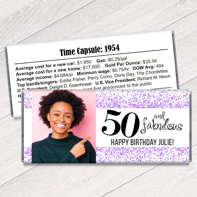 K&ouml;nnte beinhalten: Eine personalisierte Schokoriegelverpackung mit einem Foto einer Frau, dem Text "50 and fabulous" und "Happy Birthday Julie!" in schwarzer Schrift. Die Verpackung hat ein rosa-lila Konfetti-Design und einen Abschnitt mit historischen Fakten.
