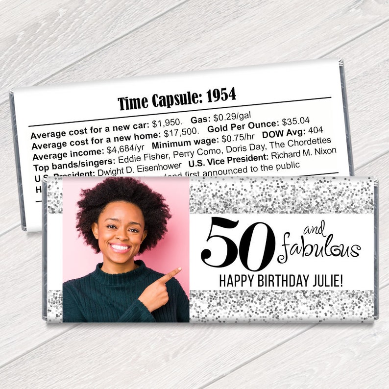 K&ouml;nnte beinhalten: Eine personalisierte Schokoriegelverpackung mit einem Foto einer Frau, dem Text "50 and fabulous" und "Happy Birthday Julie!". Die Verpackung hat ein silbernes Glitzerdesign und einen Abschnitt mit historischen Fakten von 1954.