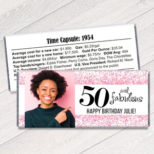 K&ouml;nnte beinhalten: Eine personalisierte Schokoriegelverpackung mit rosa Glitzerdesign und dem Text "50 and fabulous HAPPY BIRTHDAY JULIE!". Sie zeigt ein Foto einer Frau und ein "Time Capsule: 1954"-Infoblatt.