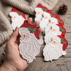 May include: A collection of embroidered Santa Claus ornaments featuring a red hat with green holly leaves and red berries, a white beard, and a tan face. Each ornament has a small loop at the top for hanging, showcasing detailed stitching.