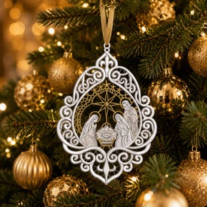 Pode incluir: Um enfeite de Natal de renda branca com uma cena de natividade com três figuras e uma estrela central. O ornamento tem uma borda intrincada de volutas e está suspenso por uma fita dourada, com bordados detalhados da sagrada família.