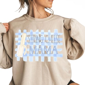 May include: A beige sweatshirt featuring the words "STRING CHEESE MAMA" in blue, set against a light blue checkered design. A string cheese graphic is also present. The sweatshirt has long sleeves.