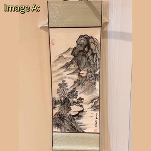 Peut inclure: Peinture de paysage asiatique traditionnelle sur un rouleau suspendu. L'œuvre représente une scène de montagne avec des arbres, une rivière et un petit bâtiment. Le rouleau a une bordure vert clair et est accroché à un cintre blanc.