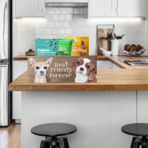 May include: A wooden sign with the text "Best Friends Forever" and illustrations of two dogs. The sign is on a wooden countertop, with dog treats in the background.