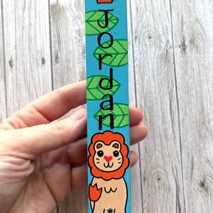 A hand is holding a colorful name tag with a cartoon lion and the name "JORDAN" written on it.