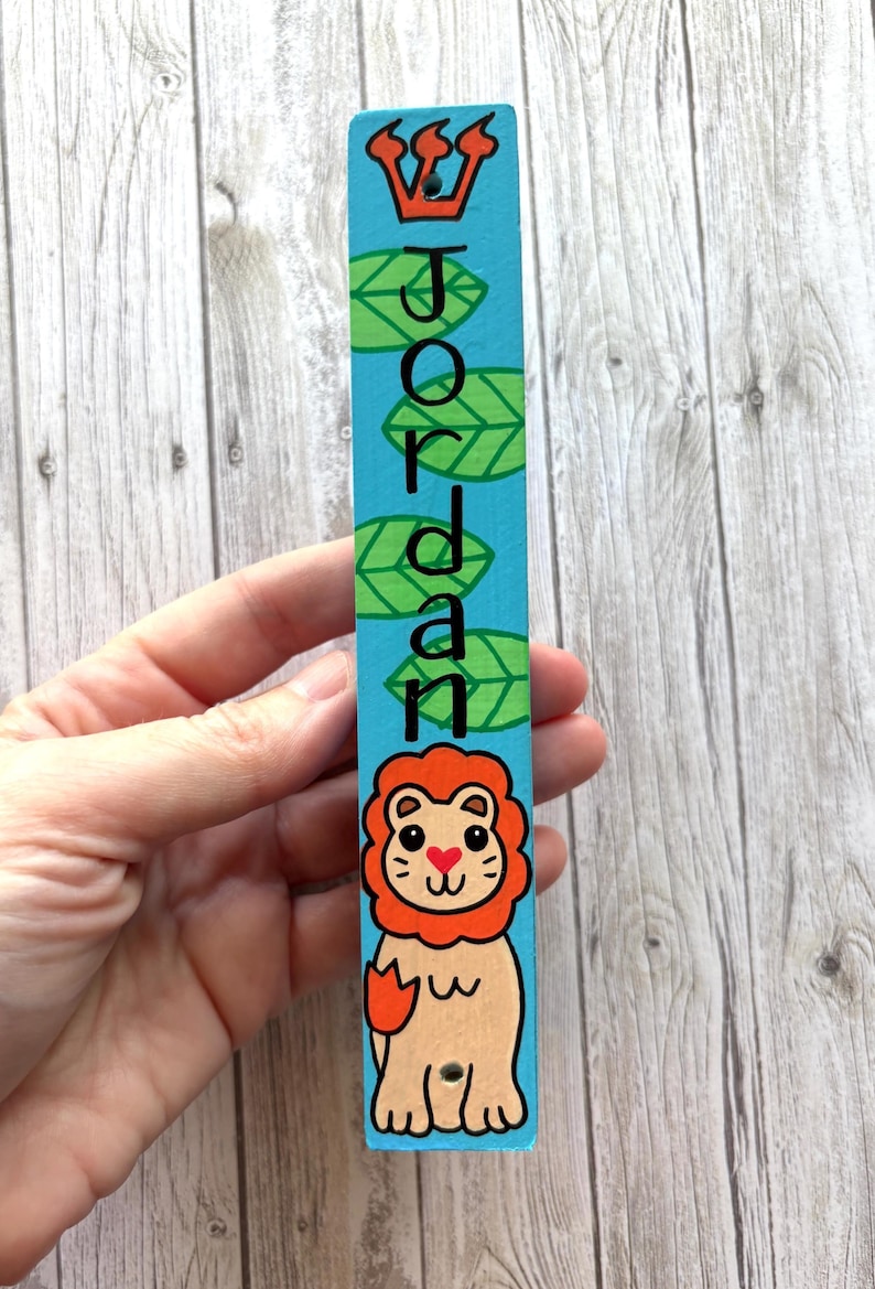 A hand is holding a colorful name tag with a cartoon lion and the name "JORDAN" written on it.