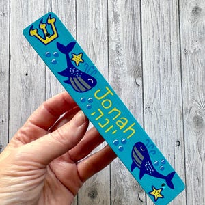 A hand is holding a blue and yellow rectangular bookmark with a crown and fish design.