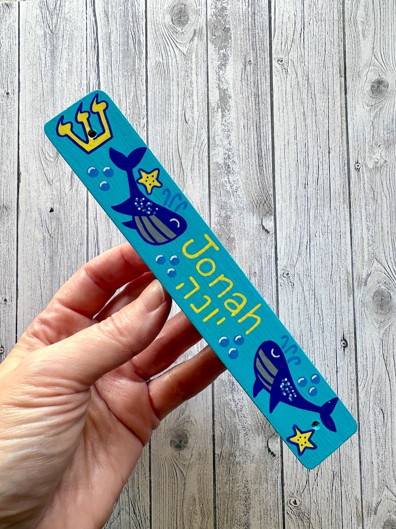 A hand is holding a blue and yellow rectangular bookmark with a crown and fish design.