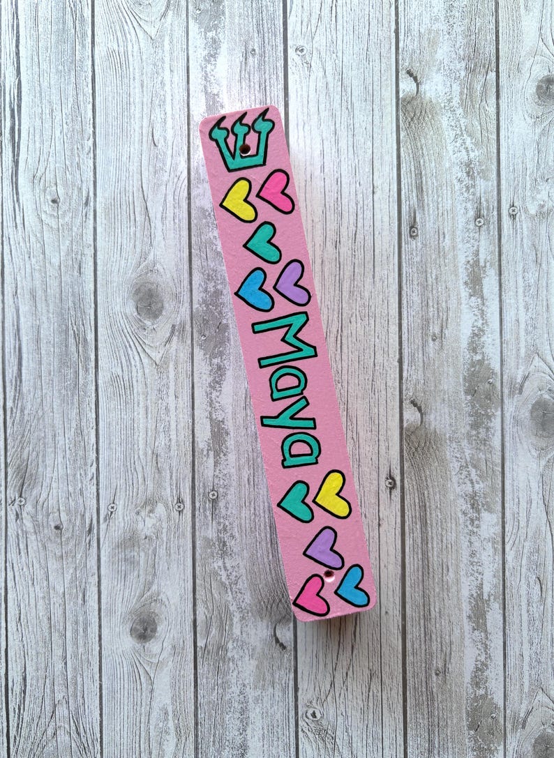 A pink bookmark with a crown and hearts on it, placed on a wooden surface.