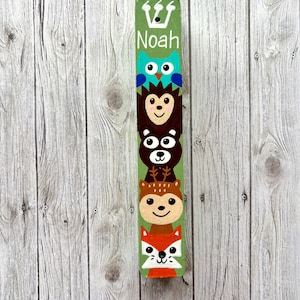 A colorful, hand-painted wooden stick with a vertical arrangement of animal faces, including a bear, owl, and fox, against a wooden background.