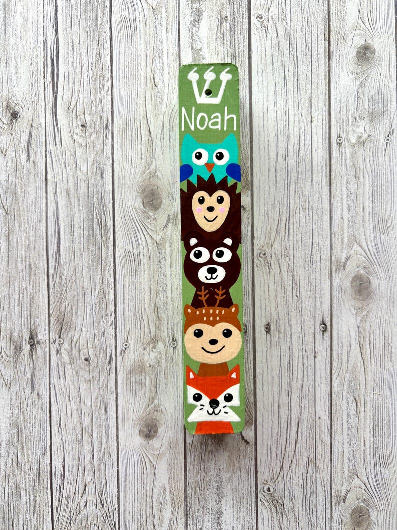 A colorful, hand-painted wooden stick with a vertical arrangement of animal faces, including a bear, owl, and fox, against a wooden background.