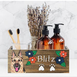 A wooden crate with a picture of a German Shepherd dog on it, along with a vase of lavender flowers and two brown bottles.