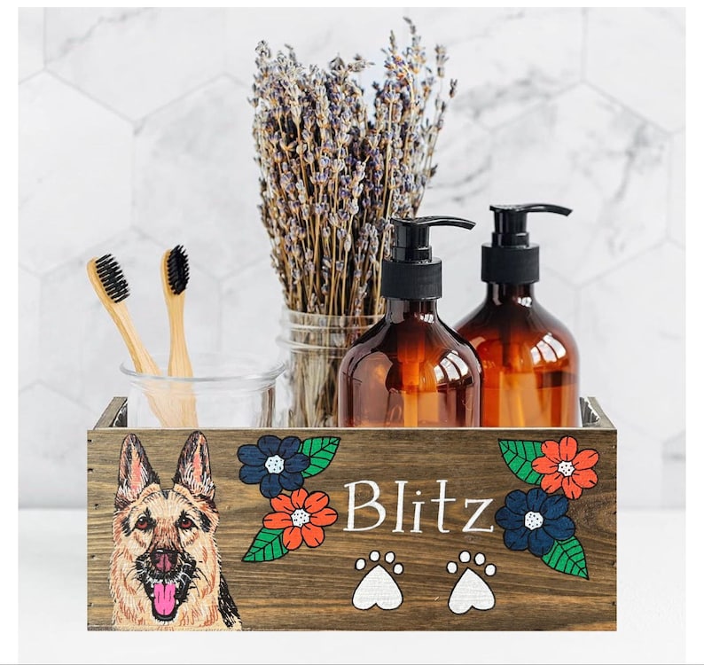 A wooden crate with a picture of a German Shepherd dog on it, along with a vase of lavender flowers and two brown bottles.