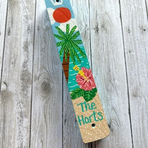 A colorful wooden stick with a tropical design, including a palm tree, flowers, and a bird, is placed on a wooden surface.
