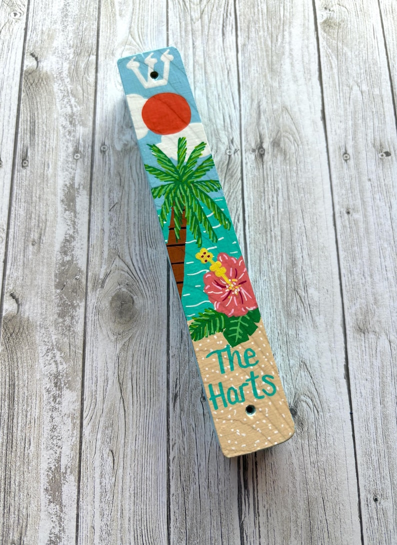 A colorful wooden stick with a tropical design, including a palm tree, flowers, and a bird, is placed on a wooden surface.