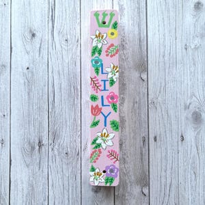 A colorful, hand-painted wooden stick or sign with floral designs and the name "Lily" written on it, placed on a wooden background.