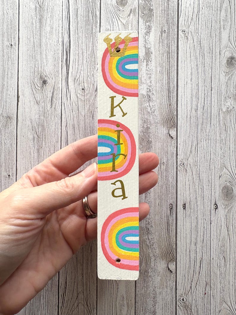A hand holding a colorful, personalized name tag with a rainbow design.