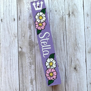 A purple sign with a crown and flowers on it, placed on a wooden surface.