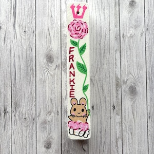 A white wooden board with a pink flower and a cartoon mouse on it, placed against a wooden background.
